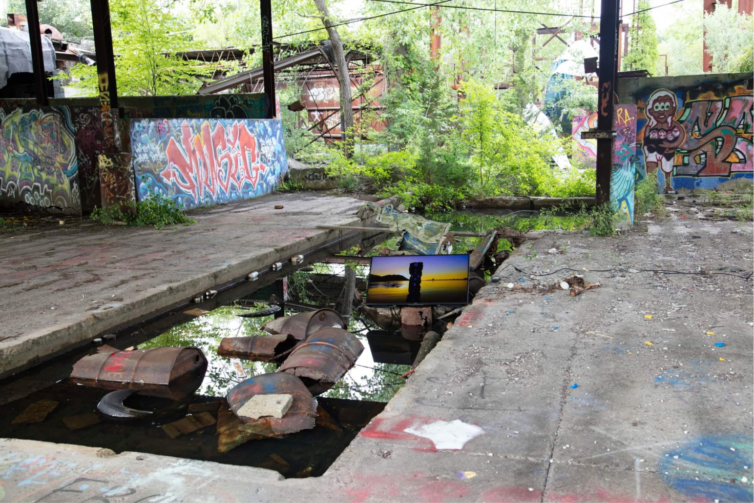 A video showing a monolith emerging from water at sunset plays on a screen installed in a trash-filled pool