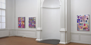 A white-walled gallery with a round niche flanked by colored abstracts prints hanging on the walls