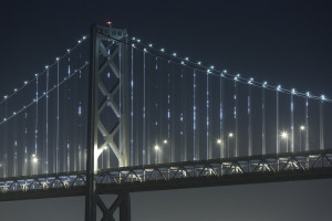 A photo of a bridge at night. The cables glow with white lights at random intervals