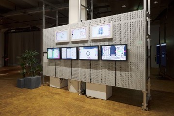 Seven rectangular monitors hang in two rows on a white pegboard wall