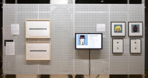 Prints and a screen hang on a pegboard, displaying various iterations of pixelated portraits