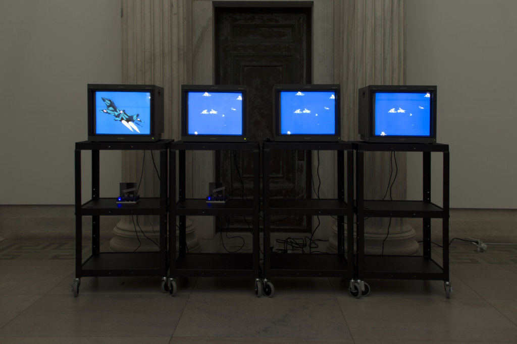 Four cathode-ray monitors on rolling stands display clouds and a fighter jet from a Nintendo game