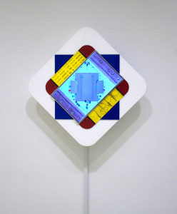 A photograph of a wall-mounted sculpture consisting of computer parts and acrylic plastic colored red, yellow, and blue