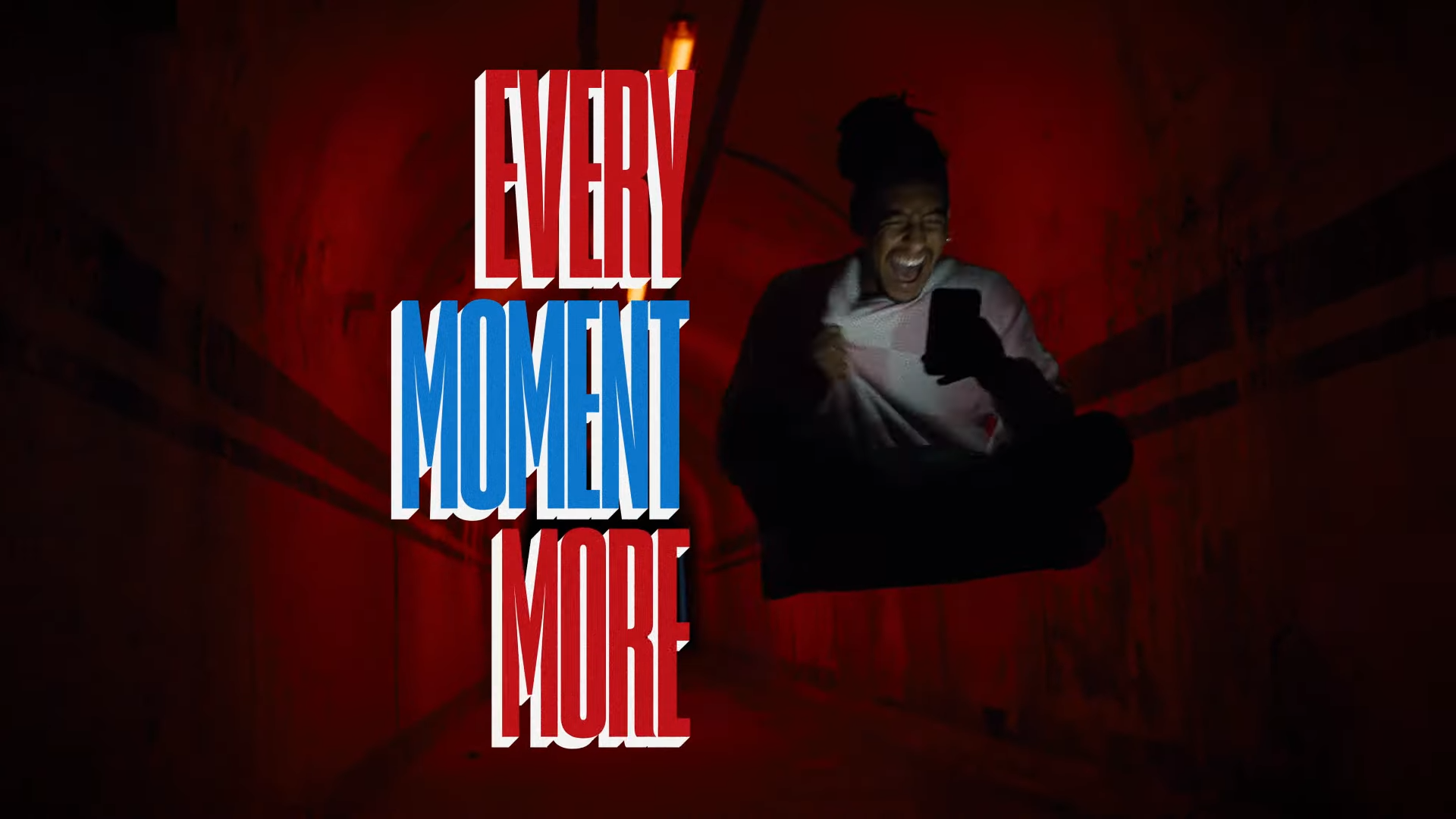 A man laughing at his phone in excitement sits next to text that says "Every Moment More"