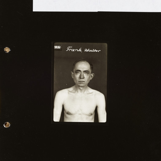 A small black-and-white portrait of a shirtless middle-aged man with his name written at the top; the photo is set on a black field with archival notes handwritten on a white strip at the top