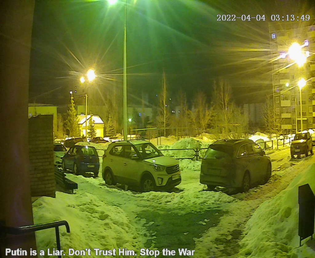 A photograph with a fisheye lens of small cars parked in a snowy back lot, with a timestamp at the upper right and the words "Putin is a Liar. Don't Trust Him. Stop the War" at the bottom left