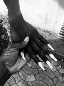 A photo of a pair holding hands, with one hand's fingers fanned out to display long white acrylic nails.