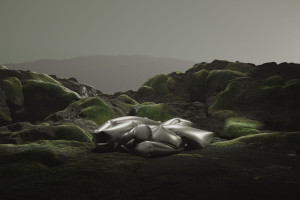 An inflated silvery form lies in messy coils amid a mossy, rocky landscape beneath a gray sky