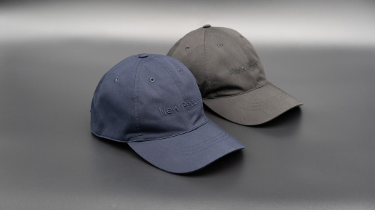 A pair of hats, one blue and one gray, with the words New Peace embroidered in the same color as the fabric