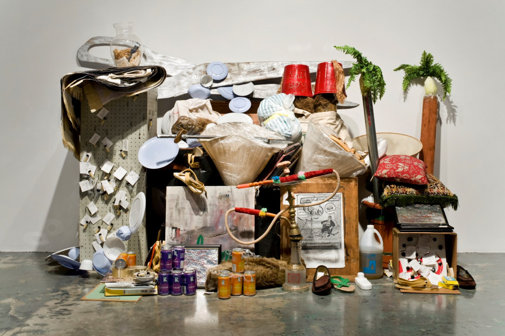 An installation of discarded furniture, plastic objects, dishware, canned soda, and other common items