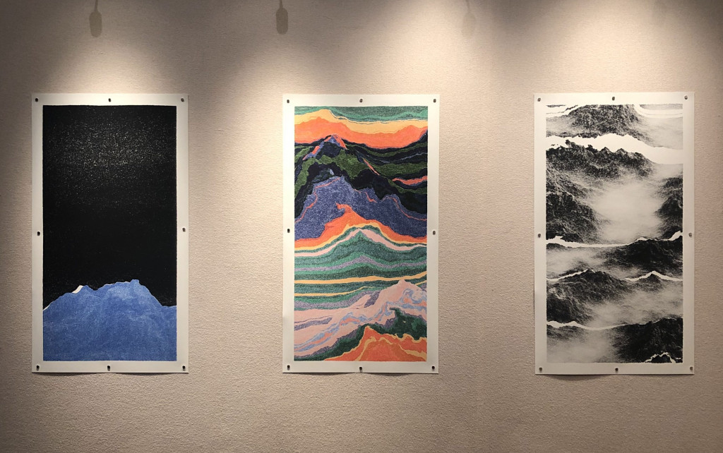 Three vertical prints showing mountainous landscapes in various colours against a beige wall