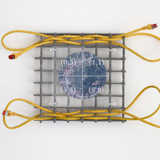 A small grey metal gridded square interwoven with a yellow Ethernet cable, overlaid with a plastic sheet showing an aerial view of a suburban landscape, hung on a white gallery wall