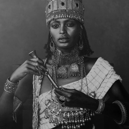 A black-and-white photograph shows a glamorous Black woman decked out in golden jewels and a crown