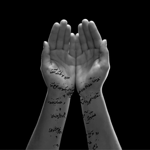 A pair of hands opening to reveal Arabic calligraphy inscribed on the wrists and forearms, softly lit against a black background