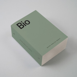 A thick book with a solid pale green cover, placed on a white table