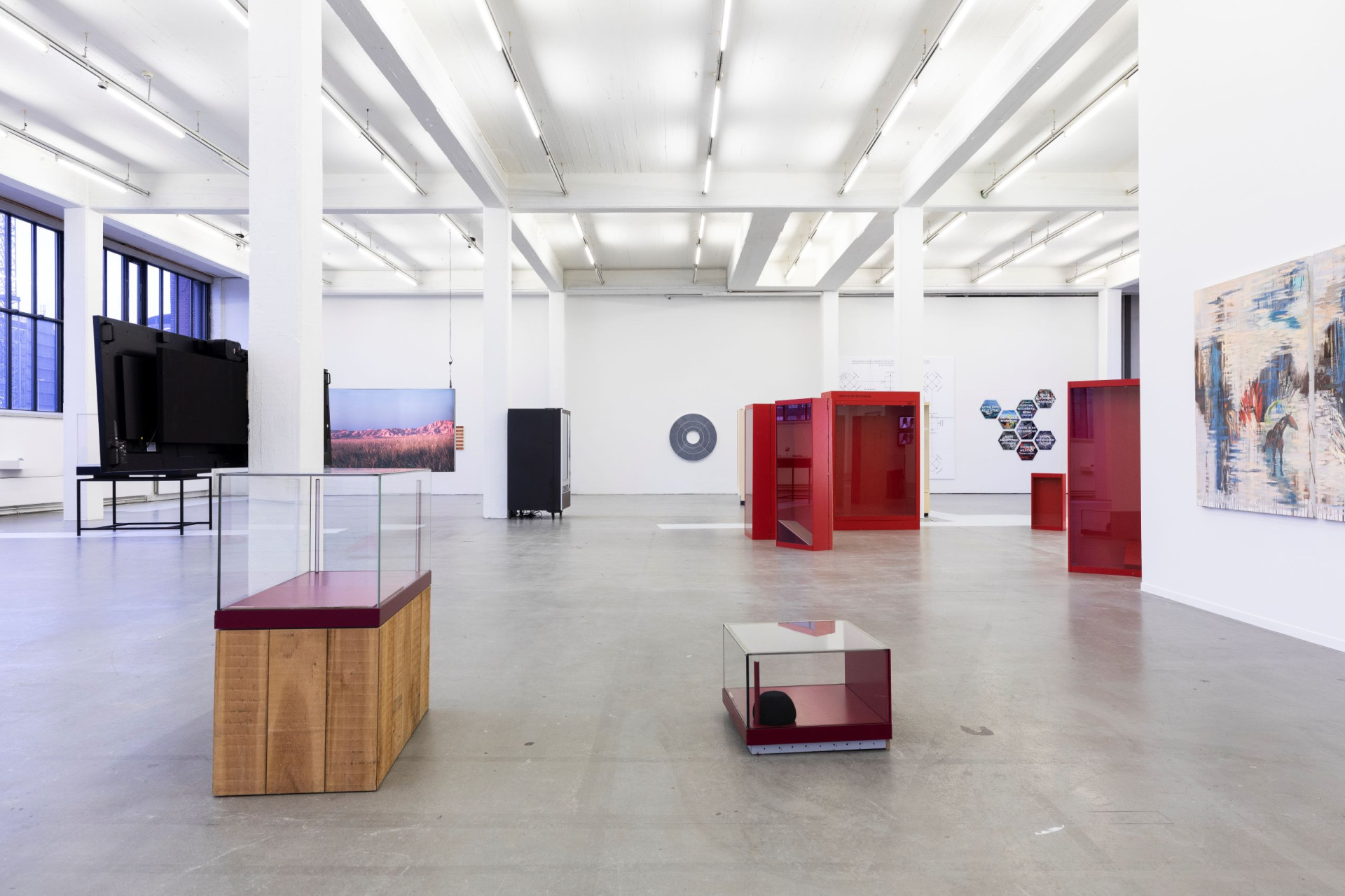 A view of an exhibition where various vitrines and metallic, boxlike sculptures occupy a spacious, airy gallery