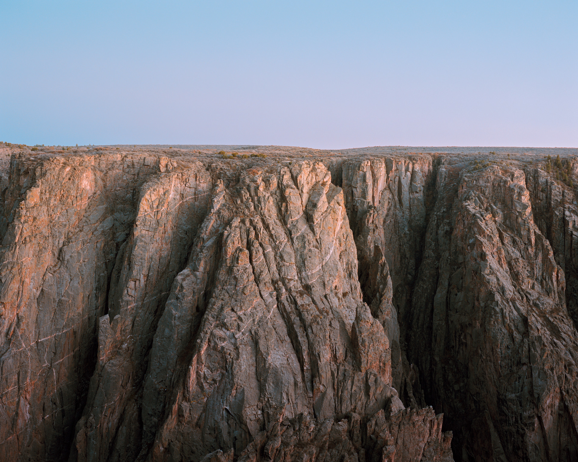 A photograph of a rugged rock formation, flat on the top where it meets the blue sky