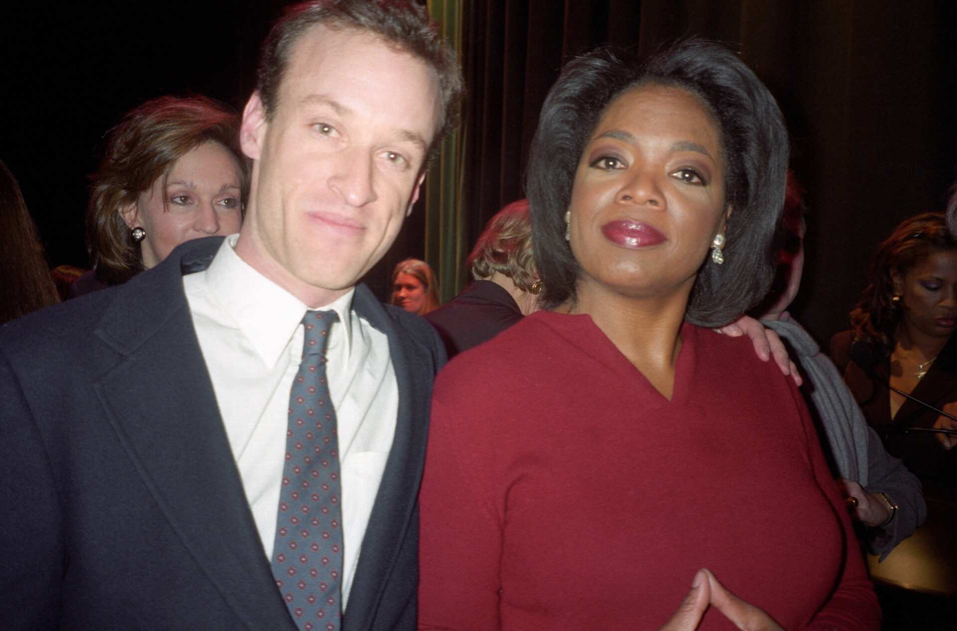 A photo of a white man in a grey suit posed next to Oprah Winfrey