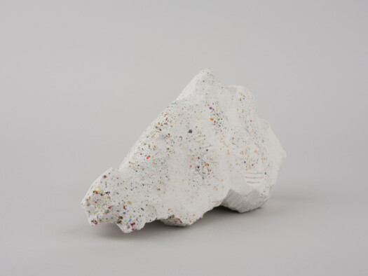 A white rock dappled with rainbow-colored spots sits in a white room