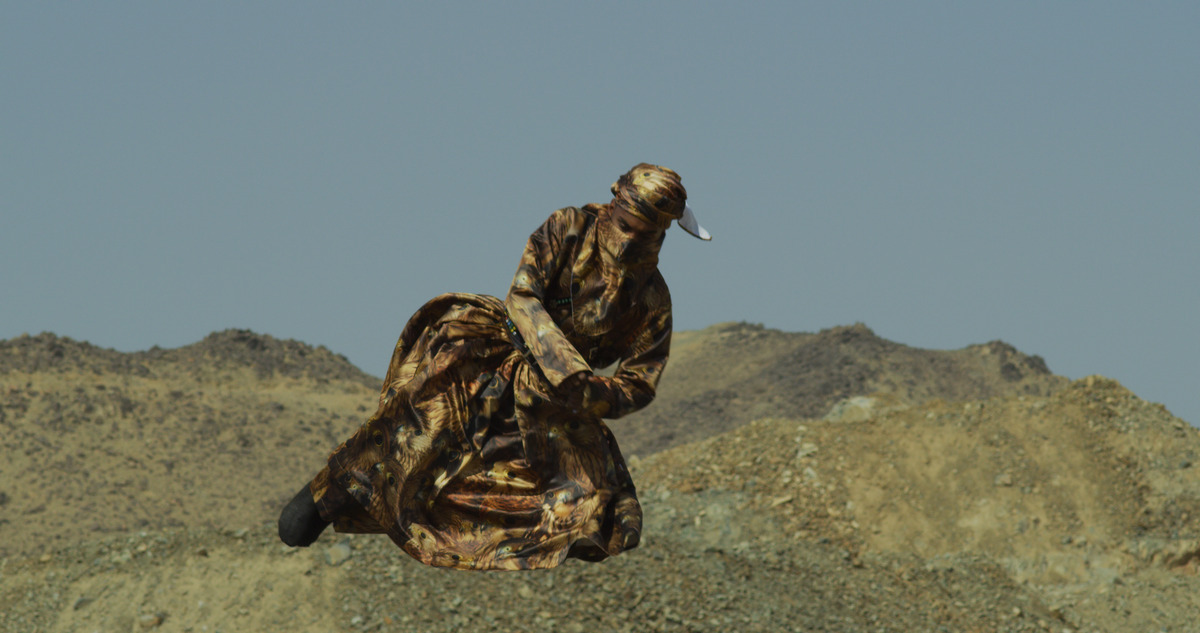 A man wearing robes printed with images of falcons dances in the desert