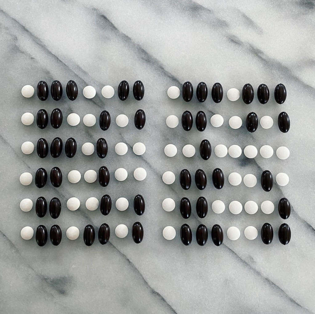 A photo of black and white pills lined up in a grid, on a marble countertop